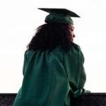 A graduate in a cap and gown looks out over a balcony